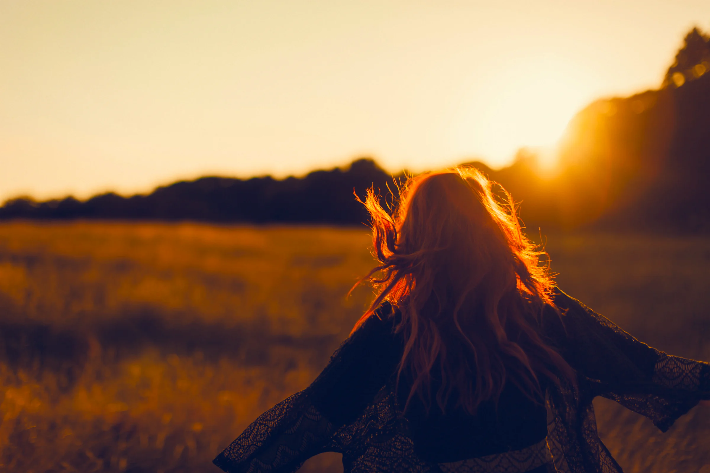 A woman in a meadow at sunset, her hair lit from behind by the low sun. Developed in NOISO. with the Golden look at 60% strength.